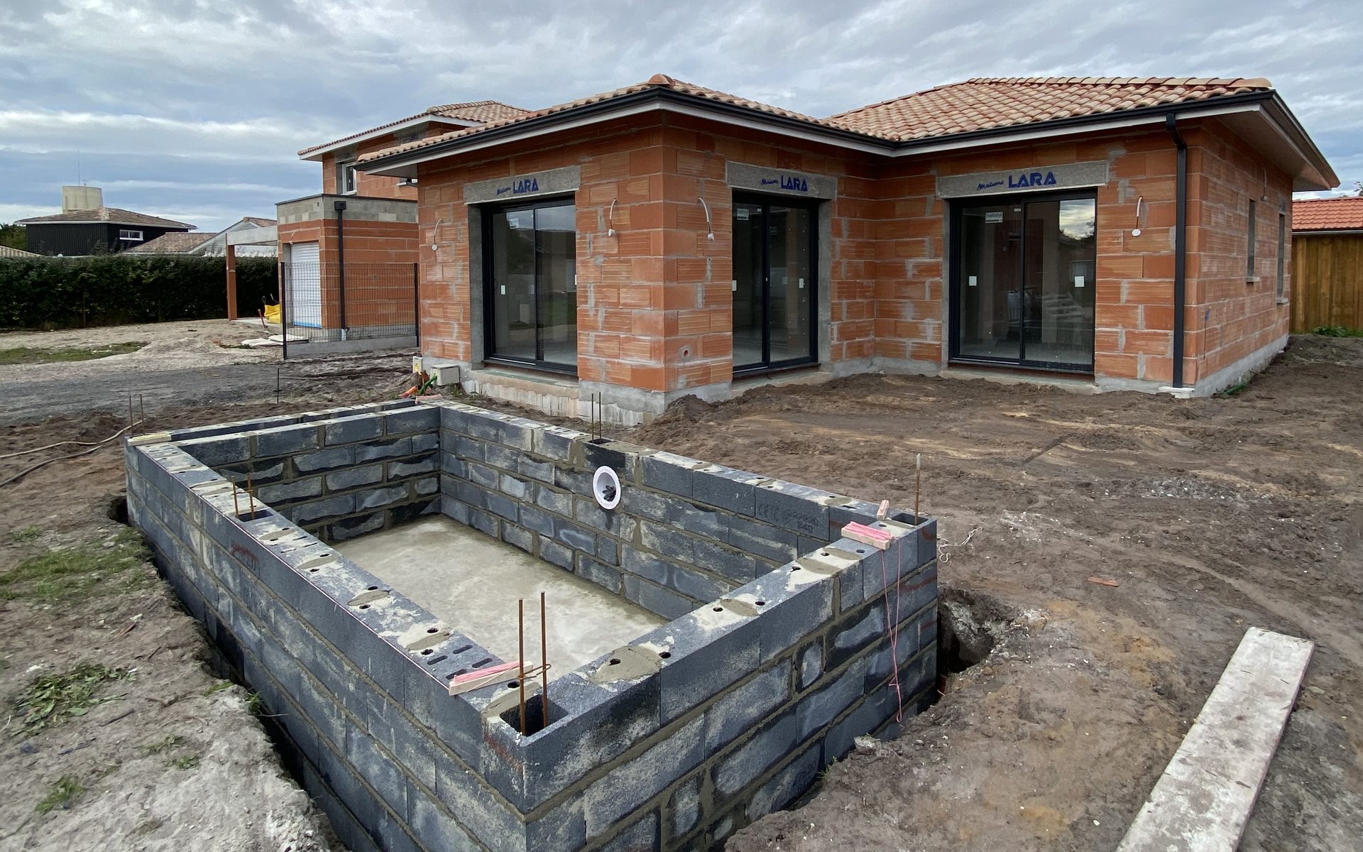 Bassin de piscine maçonnée en blocs béton en cours de construction devant une maison neuve